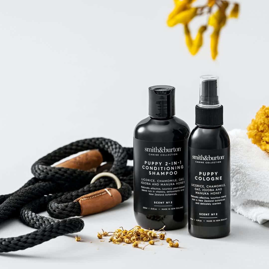 Two black bottles of Smith & Burton pet care products on a light surface with a leash and flowers in the background.