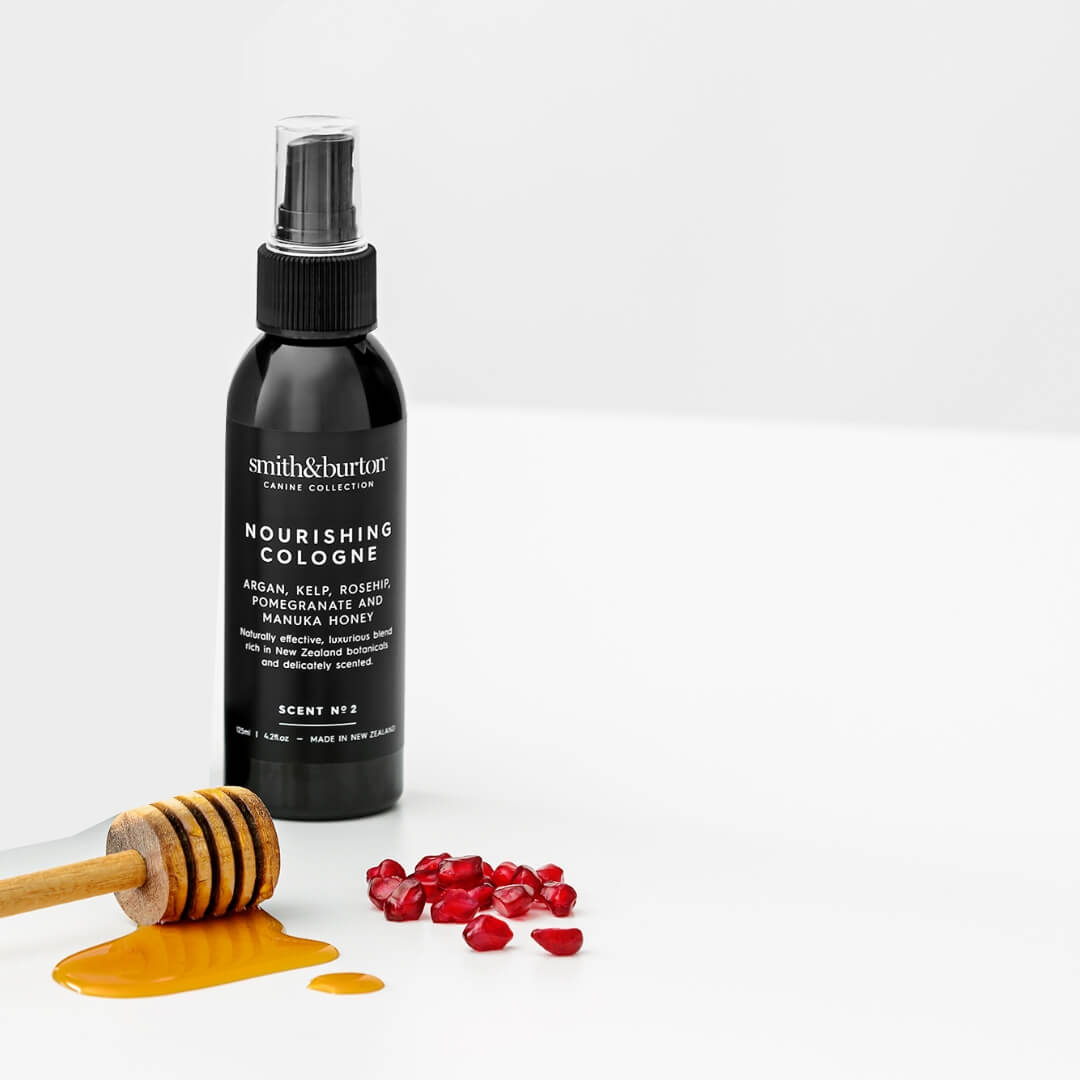 Black bottle of Smith & Burton Nourishing Cologne with honeycomb and red berries on a white background